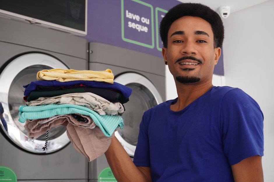 ブラジルのペルナンブコ州にあるコインランドリーで、洗いたての服を抱える幸せそうな男性。