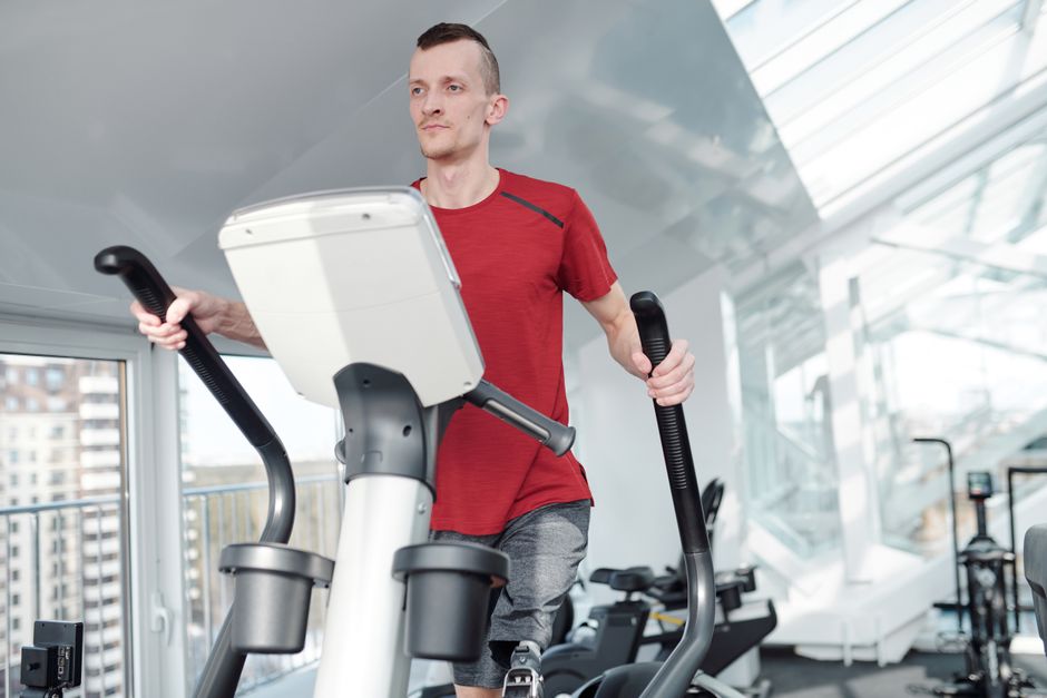 明るく現代的なジムでエリプティカルトレーナーでトレーニングをする義足の男性。