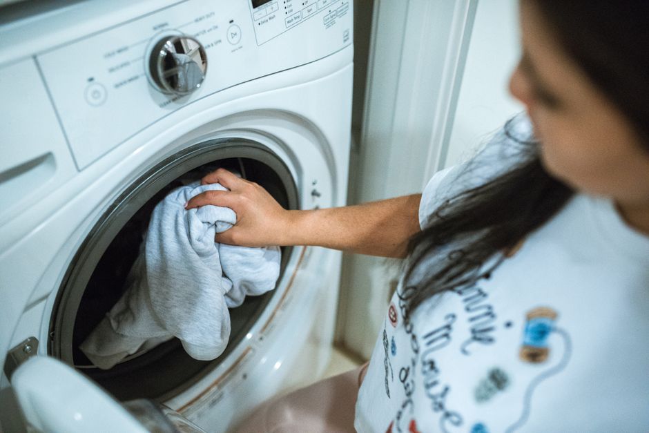 白いフロントロード洗濯機の前に立っている灰色のシャツの女性