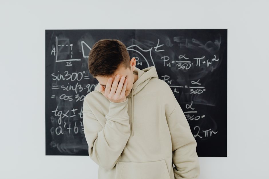 三角法の方程式でいっぱいの黒板の前に立つ、フラストレーションを抱えた教室の学生。