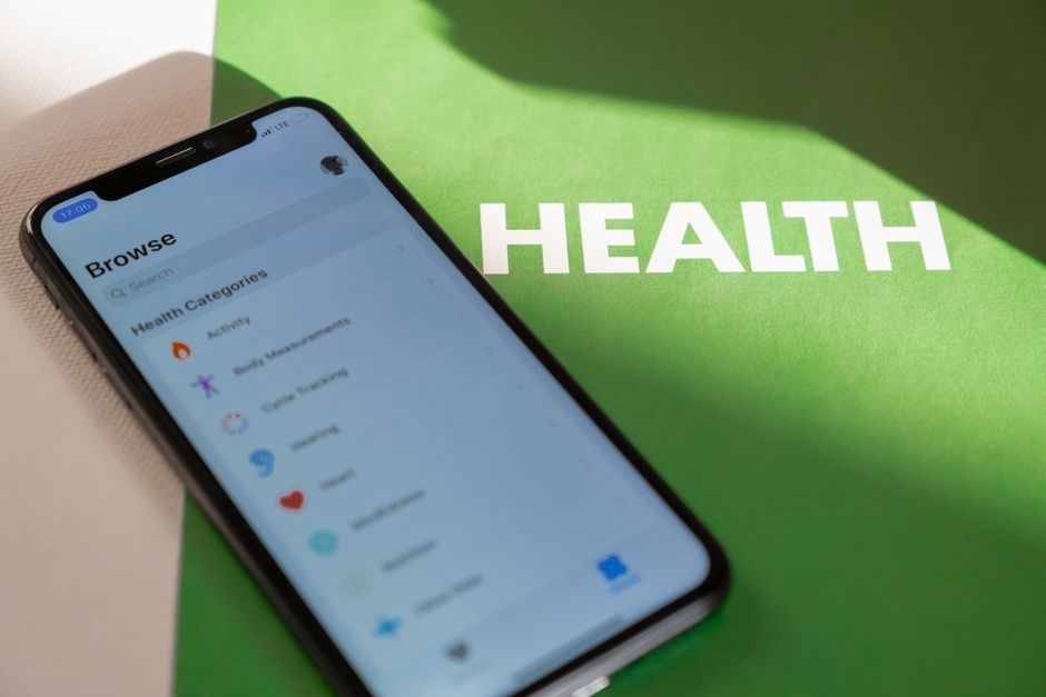 緑の表面に健康アプリを表示しているスマートフォンのクローズアップと'健康'というテキスト。