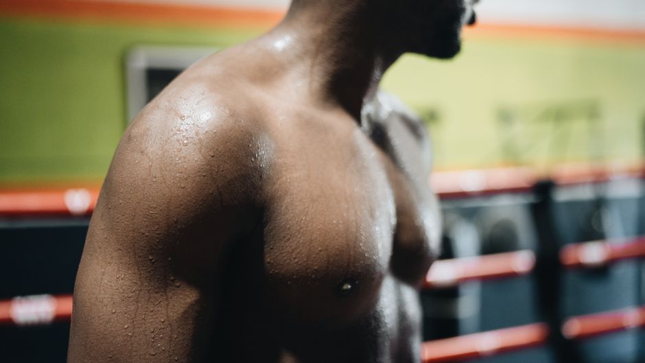 汗をかいて筋肉質の男性が室内で運動し、強さとフィットネスを披露しています。