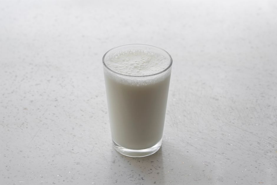 テクスチャーのある白い表面の上にある泡立った牛乳のグラスを、ミニマリズムで捉えました。