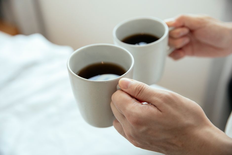 熱い黒いコーヒーが入った2つのマグを持つ手のクローズアップ、心地よい朝にぴったりです。